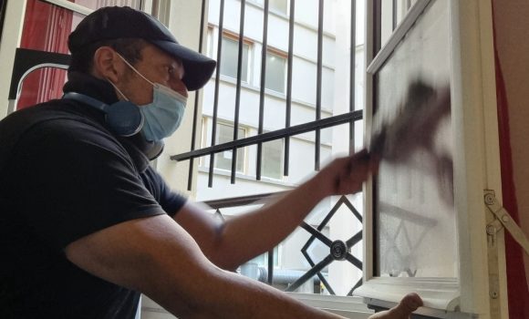 Un homme professionnel en tenue de travail, à genoux, nettoyant avec soin une grande vitre dans une maison de particulier