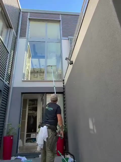 Un technicien ISOCLEAN nettoie une grande vitre à la perche depuis une cour.