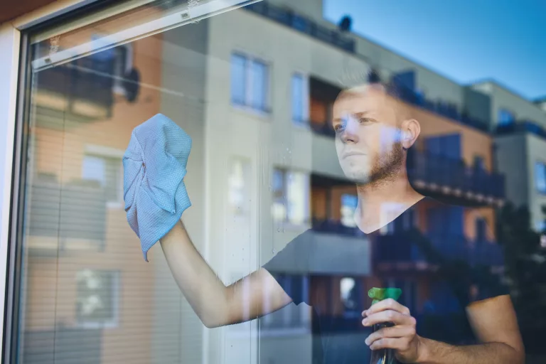 Homme nettoyant une fenêtre avec un chiffon et un spray nettoyant à domicile.
