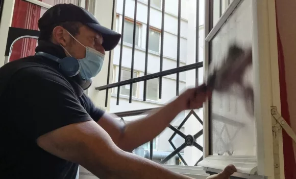 Un homme professionnel en tenue de travail, à genoux, nettoyant avec soin une grande vitre dans une maison de particulier